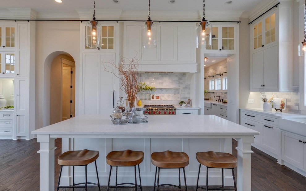 This is an example of a large traditional kitchen in Minneapolis with a farmhouse sink, white cabinets, quartzite benchtops, ceramic splashback, stainless steel appliances, dark hardwood floors, with island, shaker cabinets, multi-coloured splashback and brown floor.