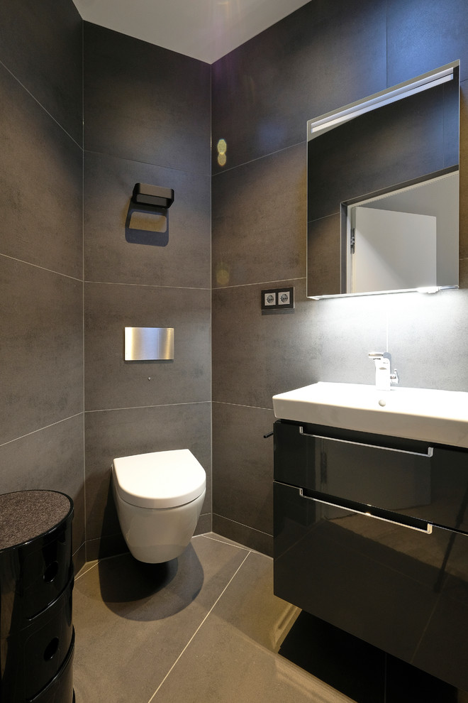 Kleines Modernes Duschbad mit flächenbündigen Schrankfronten, schwarzen Schränken, Wandtoilette mit Spülkasten, grauen Fliesen, grauer Wandfarbe, grauem Boden, bodengleicher Dusche, Unterbauwaschbecken, Schiebetür-Duschabtrennung und schwarzer Waschtischplatte in Dortmund