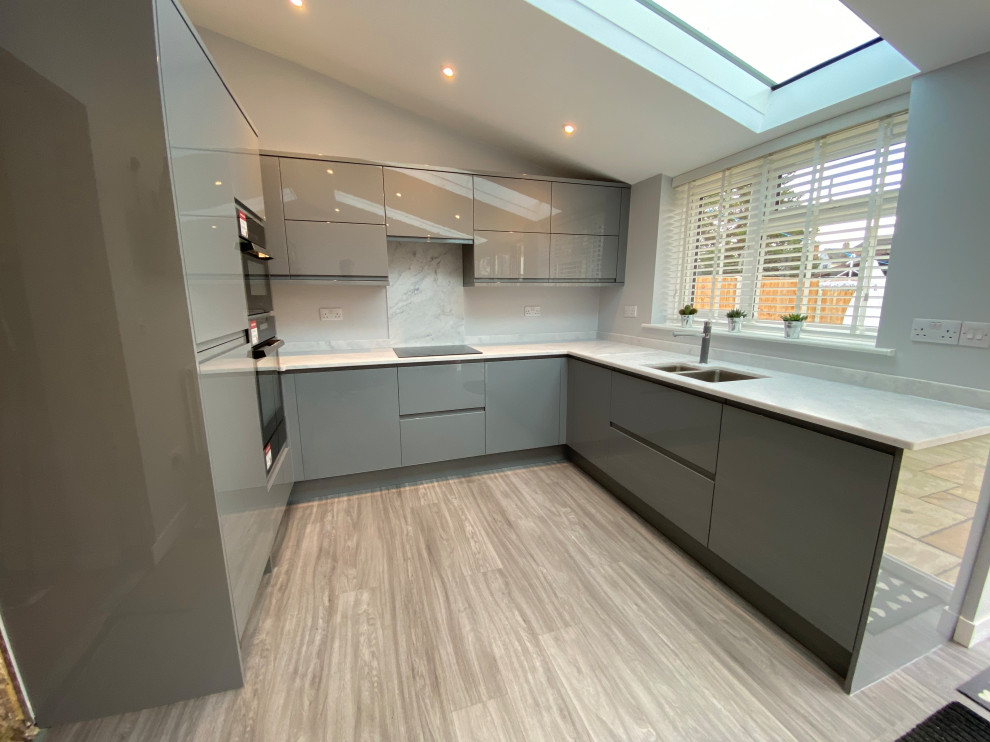 Inspiration for a medium sized contemporary grey and brown u-shaped open plan kitchen in Other with an integrated sink, flat-panel cabinets, grey cabinets, composite countertops, white splashback, integrated appliances, vinyl flooring, no island, brown floors, white worktops, a vaulted ceiling and feature lighting.