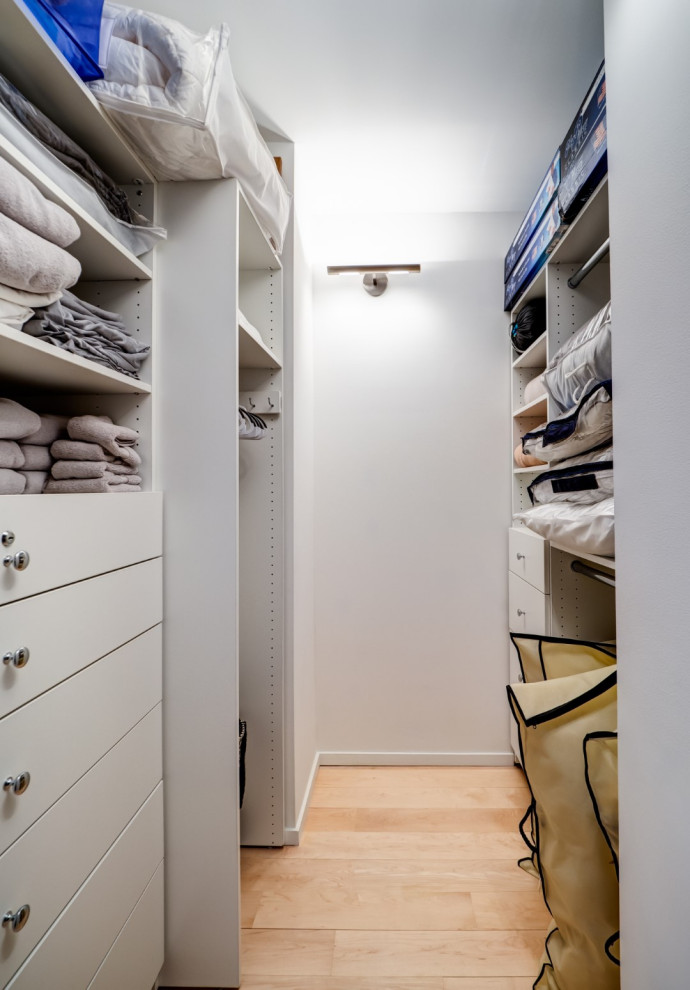 Photo of a small contemporary gender-neutral storage and wardrobe in New York with flat-panel cabinets, white cabinets, light hardwood floors and yellow floor.