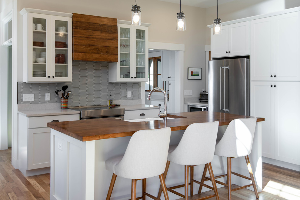 Inspiration for a rustic medium tone wood floor kitchen remodel with a farmhouse sink, white cabinets, gray backsplash, stainless steel appliances, an island, gray countertops and shaker cabinets