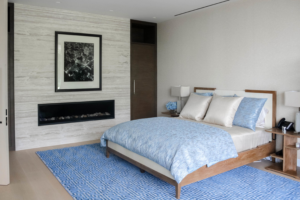 This is an example of a mid-sized contemporary master bedroom in Los Angeles with beige walls, light hardwood floors, a ribbon fireplace, a stone fireplace surround and beige floor.