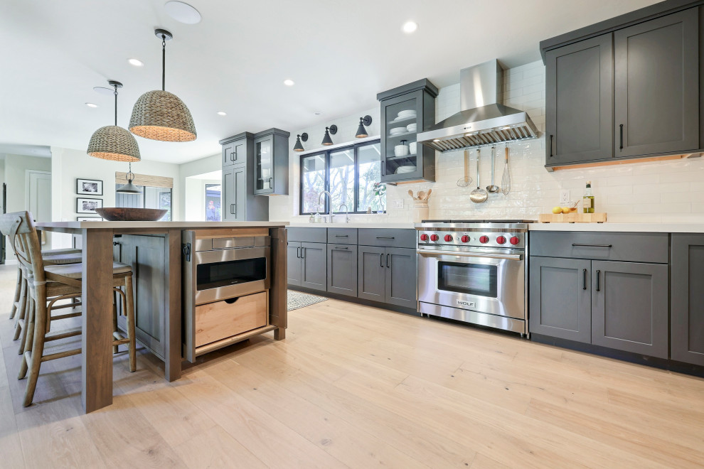 Example of a mid-sized transitional l-shaped laminate floor open concept kitchen design with a double-bowl sink, flat-panel cabinets, gray cabinets, quartz countertops, white backsplash, ceramic backsplash, stainless steel appliances, an island and white countertops