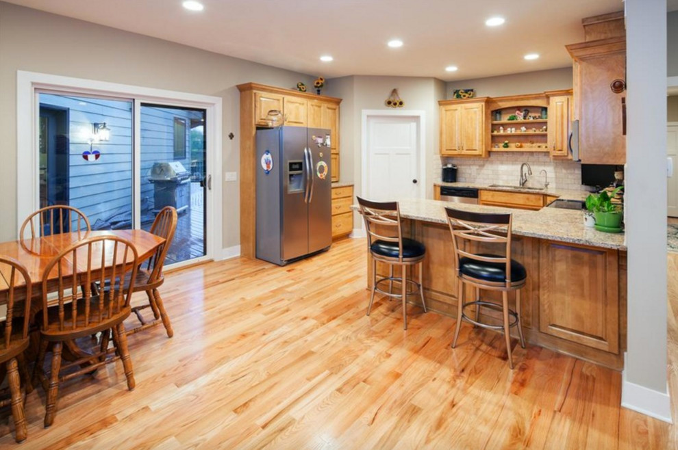 Design ideas for a mid-sized traditional u-shaped open plan kitchen in Omaha with a double-bowl sink, raised-panel cabinets, light wood cabinets, granite benchtops, white splashback, subway tile splashback, stainless steel appliances, light hardwood floors and a peninsula.