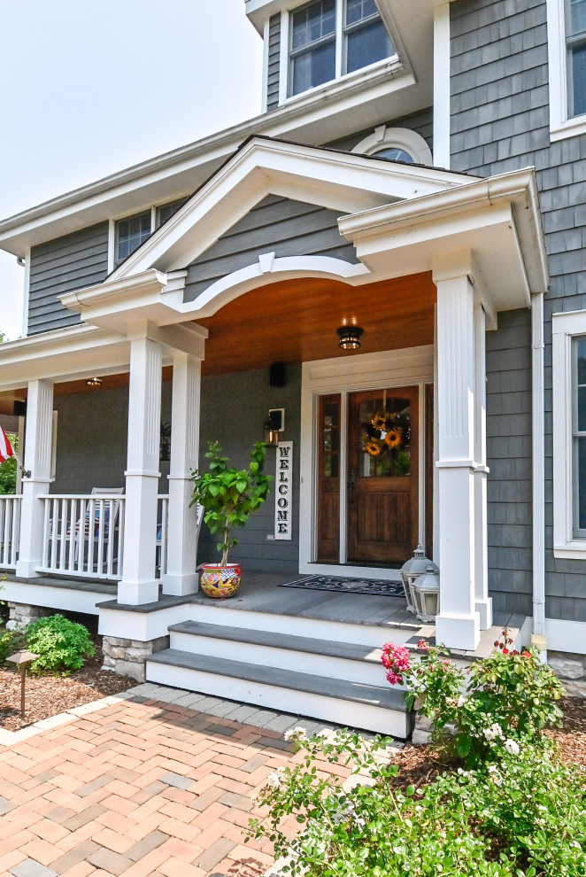 This is an example of a mid-sized transitional front yard verandah in Milwaukee with with columns, brick pavers, a roof extension and wood railing.