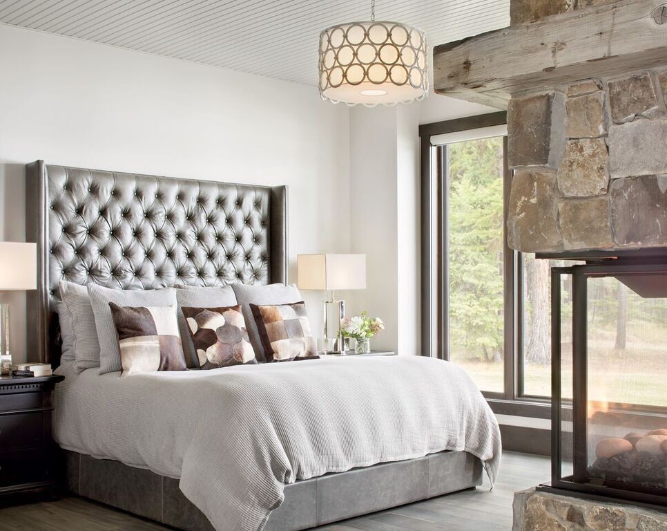 Photo of a mid-sized country master bedroom in Other with white walls, medium hardwood floors, a two-sided fireplace, a stone fireplace surround and grey floor.