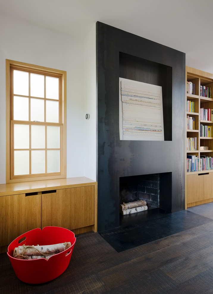Contemporary home office in San Francisco with a library, white walls, dark hardwood floors, a standard fireplace, a metal fireplace surround, a freestanding desk and black floor.