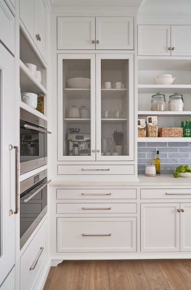 Kitchen pantry in Charlotte with a farmhouse sink, beaded inset cabinets, white cabinets, marble benchtops, white splashback, marble splashback, stainless steel appliances, medium hardwood floors, multiple islands, brown floor, white benchtop and timber.