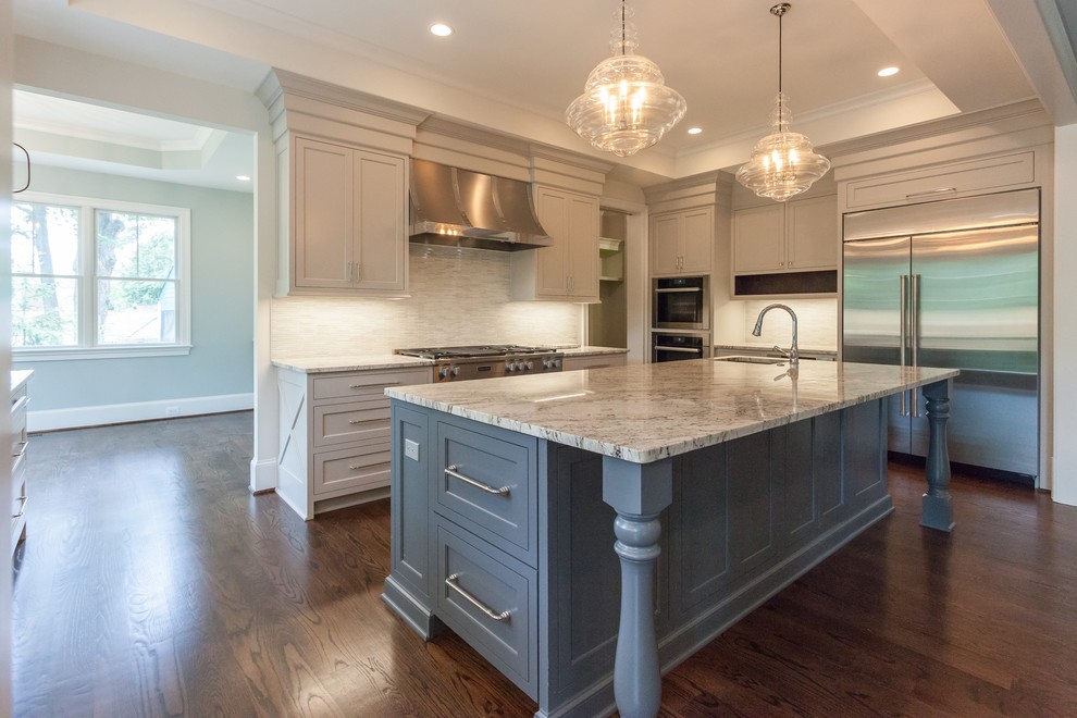 This is an example of a traditional u-shaped open plan kitchen in DC Metro with an undermount sink, beaded inset cabinets, beige cabinets, beige splashback, stainless steel appliances, medium hardwood floors, with island, brown floor and black benchtop.