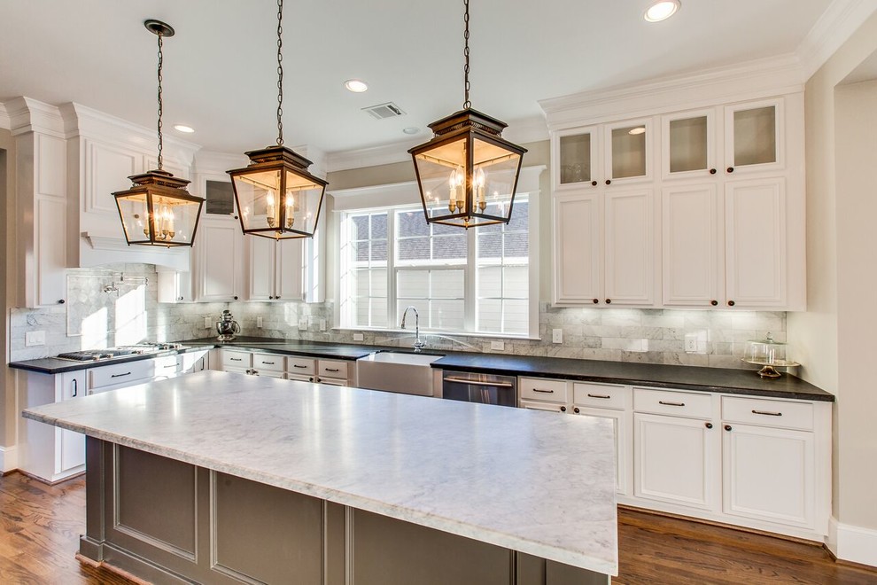 Photo of a large traditional l-shaped eat-in kitchen in Houston with a farmhouse sink, recessed-panel cabinets, white cabinets, marble benchtops, grey splashback, stone tile splashback, stainless steel appliances, medium hardwood floors, with island and brown floor.