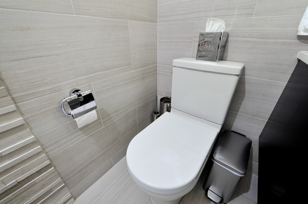 This is an example of a mid-sized contemporary bathroom in New York with an integrated sink, flat-panel cabinets, black cabinets, solid surface benchtops, an alcove tub, a shower/bathtub combo, a two-piece toilet, gray tile and beige walls.