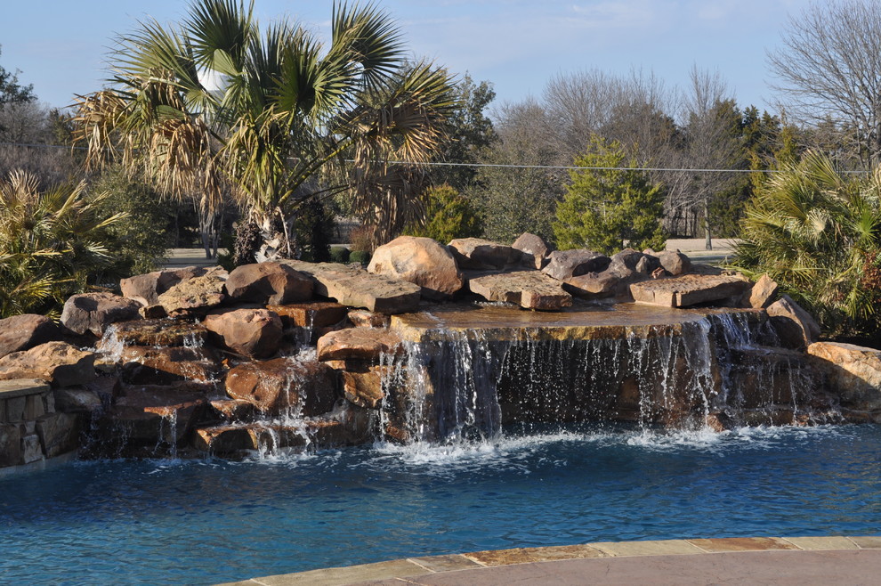 Large tropical backyard custom-shaped natural pool in Dallas with natural stone pavers.