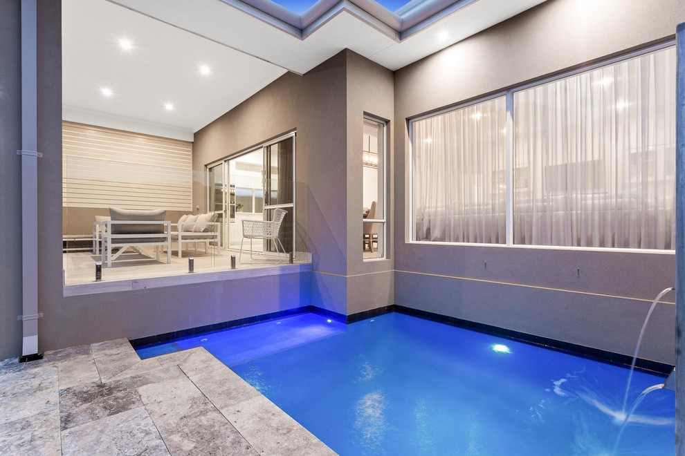 This is an example of a small beach style backyard custom-shaped pool in Perth with a water feature and natural stone pavers.