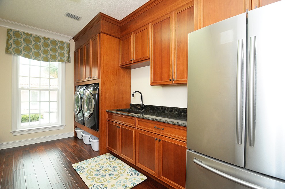 This is an example of a large transitional single-wall utility room in Tampa with an undermount sink, recessed-panel cabinets, medium wood cabinets, dark hardwood floors, a side-by-side washer and dryer and beige walls.