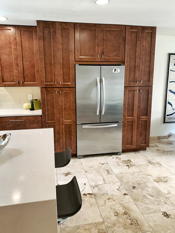 This is an example of a mid-sized transitional l-shaped eat-in kitchen in Phoenix with an undermount sink, shaker cabinets, medium wood cabinets, quartz benchtops, beige splashback, glass tile splashback, stainless steel appliances, travertine floors, with island, beige floor and white benchtop.