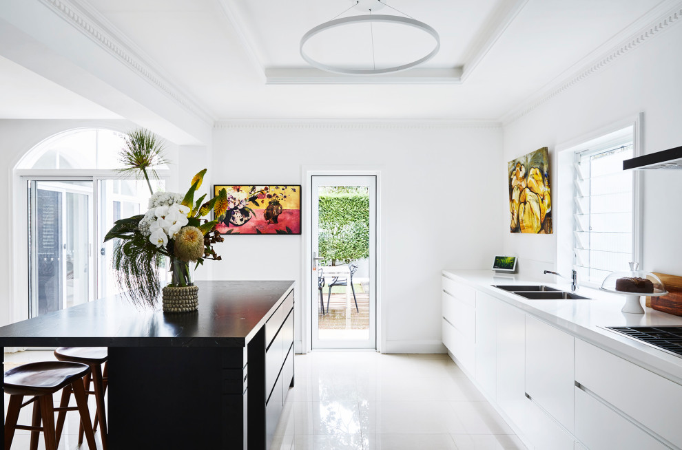 Design ideas for a large midcentury l-shaped open plan kitchen in Sydney with flat-panel cabinets, white cabinets, granite benchtops, white splashback, cement tiles, with island, white floor and black benchtop.