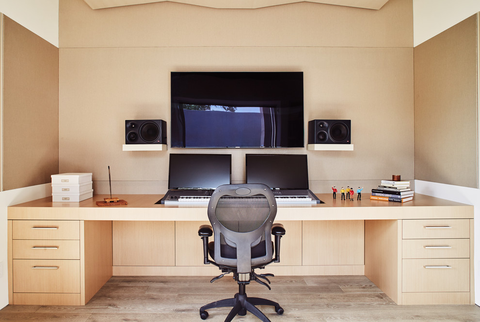 This is an example of a modern home office in Los Angeles with beige walls, light hardwood floors, a built-in desk and beige floor.