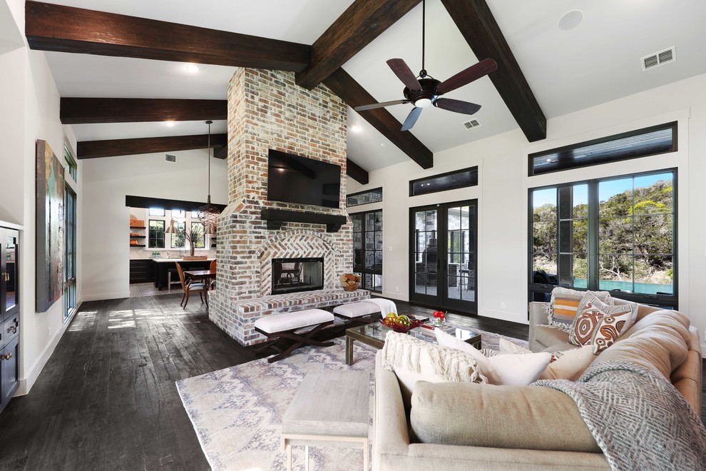 This is an example of a transitional open concept family room in Austin with white walls, dark hardwood floors, a two-sided fireplace, a brick fireplace surround, a wall-mounted tv and black floor.