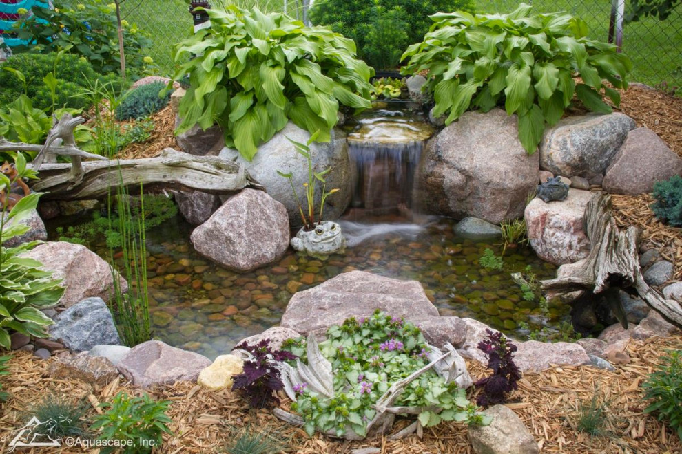 Foto di un piccolo giardino formale mediterraneo esposto in pieno sole dietro casa in estate con una cascata e sassi di fiume