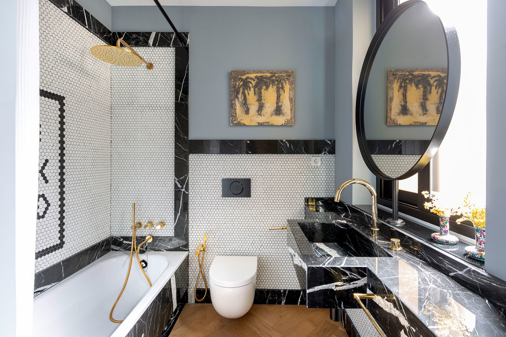 Contemporary 3/4 bathroom in Other with a drop-in tub, a shower/bathtub combo, a wall-mount toilet, black and white tile, white tile, mosaic tile, grey walls, medium hardwood floors, an integrated sink, marble benchtops, brown floor, a shower curtain and black benchtops.