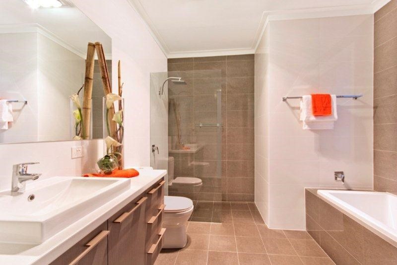 Photo of a mid-sized contemporary master bathroom in Adelaide with a drop-in sink, flat-panel cabinets, light wood cabinets, laminate benchtops, a drop-in tub, an open shower, a one-piece toilet, gray tile, porcelain tile, white walls and porcelain floors.