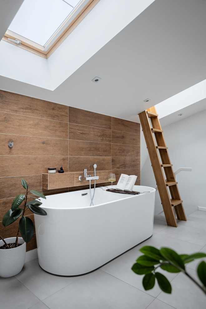 На фото: ванная комната среднего размера, в белых тонах с отделкой деревом в скандинавском стиле с отдельно стоящей ванной, коричневой плиткой, керамогранитной плиткой, полом из керамогранита и серым полом