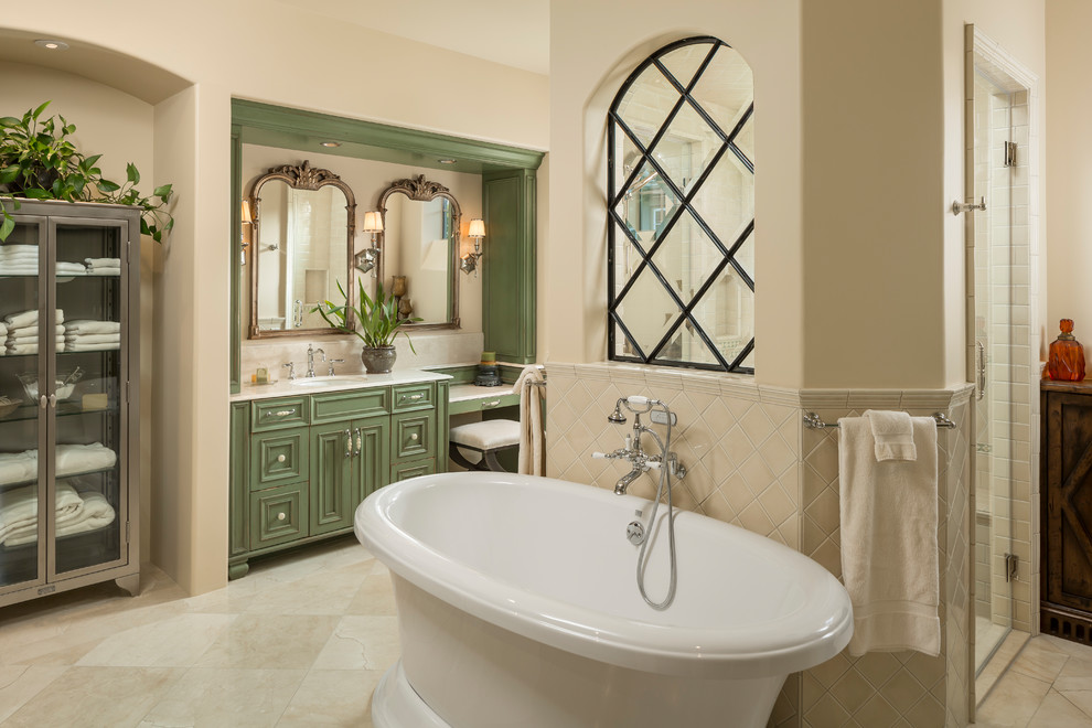 Large traditional master bathroom in Phoenix with green cabinets, a freestanding tub, beige tile, beige walls, an undermount sink, beige floor, a hinged shower door, beige benchtops, a double shower, ceramic tile, limestone floors, engineered quartz benchtops and recessed-panel cabinets.