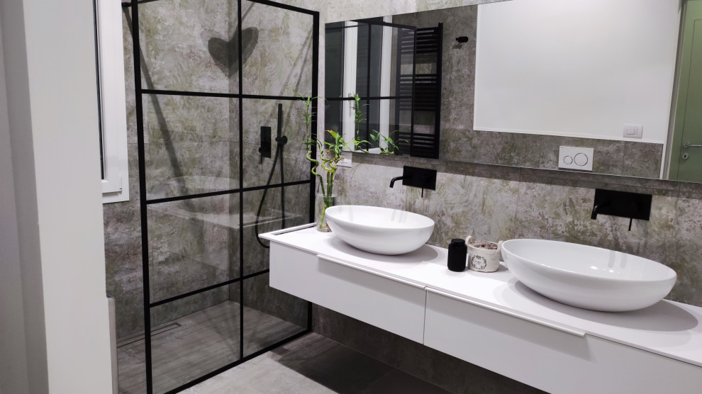 Idéer för att renovera ett mellanstort industriellt vit vitt badrum med dusch, med släta luckor, vita skåp, en kantlös dusch, en vägghängd toalettstol, flerfärgad kakel, porslinskakel, klinkergolv i porslin, ett fristående handfat och grått golv