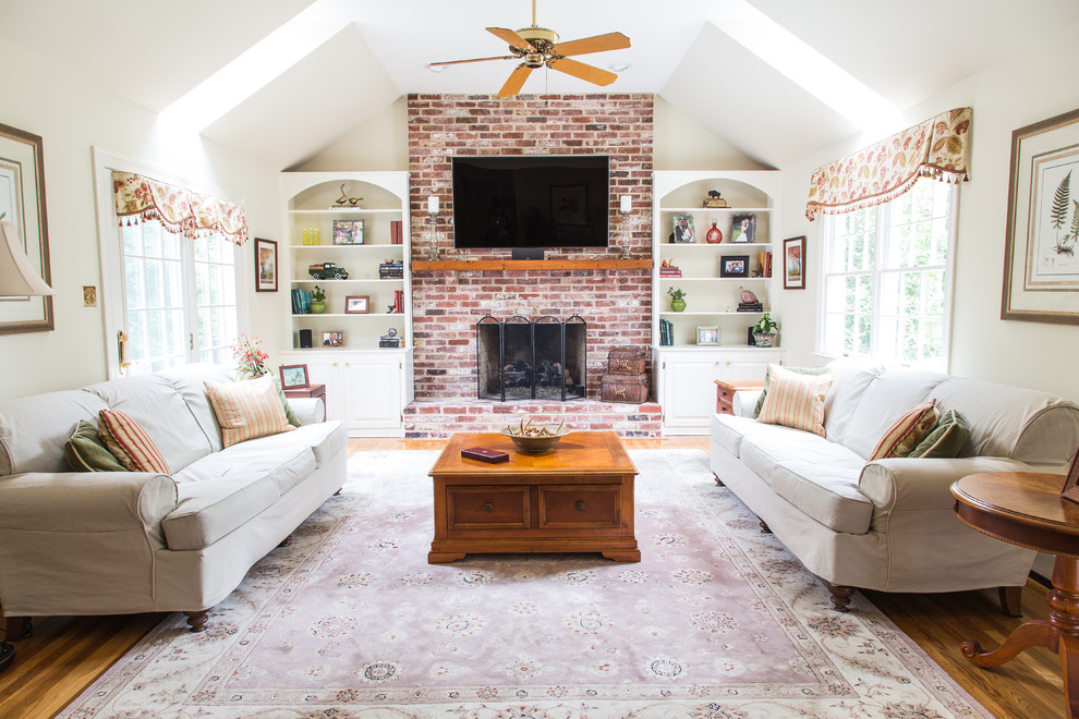 This is an example of a mid-sized country enclosed family room in Philadelphia with white walls, light hardwood floors, a standard fireplace, a brick fireplace surround, a wall-mounted tv and brown floor.