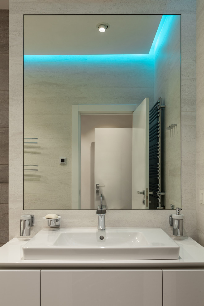 Photo of a mid-sized contemporary master wet room bathroom in Moscow with flat-panel cabinets, white cabinets, an undermount tub, a wall-mount toilet, gray tile, mirror tile, white walls, ceramic floors, a vessel sink, solid surface benchtops, grey floor, a hinged shower door and white benchtops.