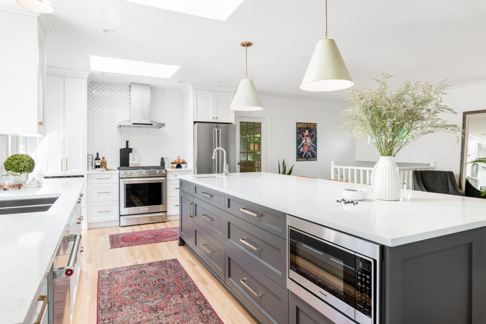 Example of a large transitional l-shaped light wood floor and beige floor open concept kitchen design in Vancouver with an undermount sink, recessed-panel cabinets, white cabinets, quartz countertops, white backsplash, ceramic backsplash, stainless steel appliances, an island and white countertops