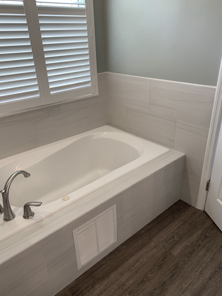 Inspiration for a mid-sized beach style master bathroom in Other with shaker cabinets, white cabinets, a drop-in tub, a corner shower, white tile, ceramic tile, blue walls, vinyl floors, an undermount sink, marble benchtops, grey floor, a hinged shower door and multi-coloured benchtops.