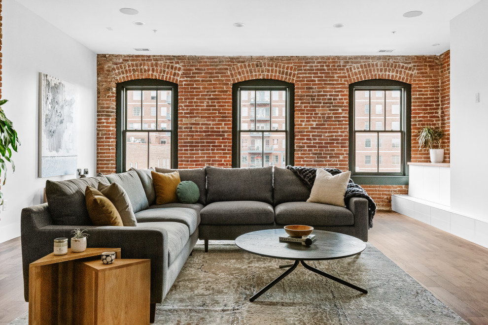 Inspiration for an industrial living room in Denver with white walls, medium hardwood floors, brown floor and brick walls.