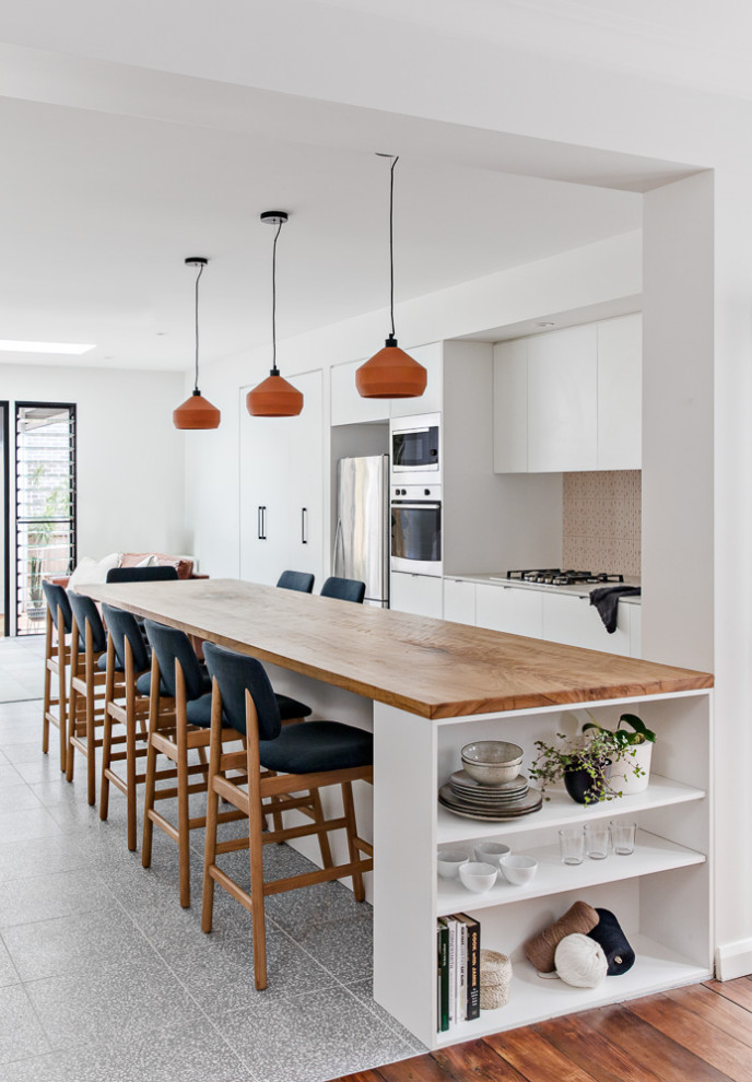 Photo of a small scandinavian galley open plan kitchen in Sydney with an undermount sink, white cabinets, wood benchtops, pink splashback, ceramic splashback, stainless steel appliances, terrazzo floors, with island, grey floor and brown benchtop.
