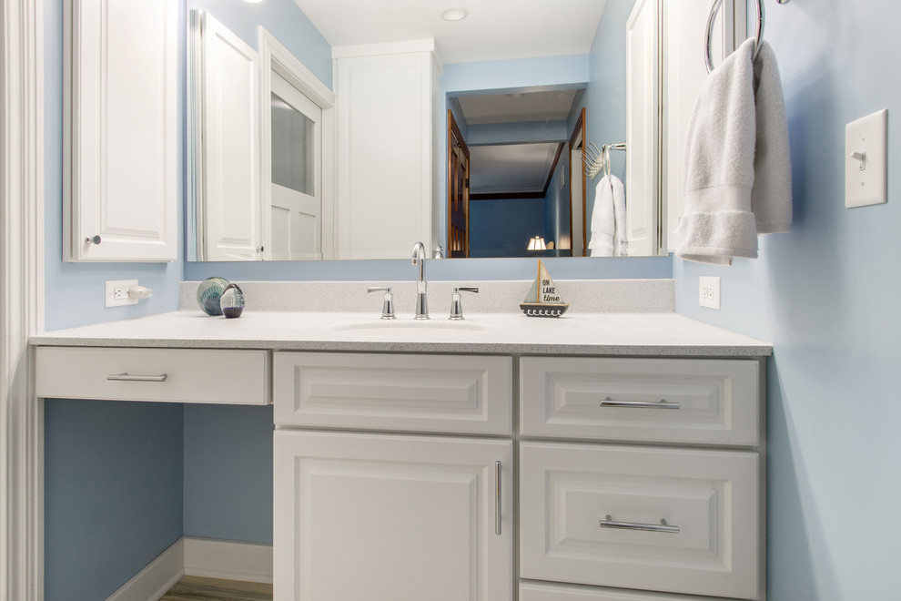 Inspiration for a mid-sized beach style 3/4 bathroom in Milwaukee with raised-panel cabinets, white cabinets, an alcove tub, an alcove shower, a one-piece toilet, blue walls, porcelain floors, an undermount sink, engineered quartz benchtops, brown floor, beige tile, a shower curtain and beige benchtops.