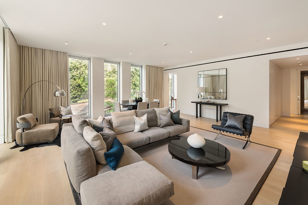 This is an example of a contemporary open concept living room in London with white walls and light hardwood floors.