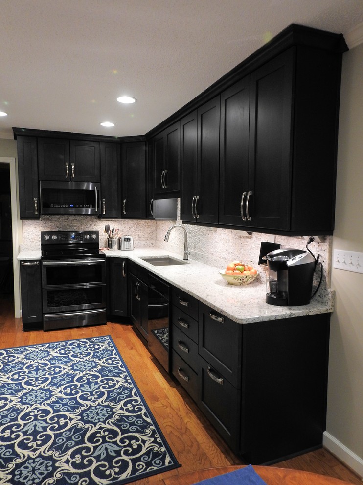Mid-sized transitional l-shaped medium tone wood floor and brown floor eat-in kitchen photo with an undermount sink, shaker cabinets, black cabinets, granite countertops, beige backsplash, stone slab backsplash, stainless steel appliances and no island