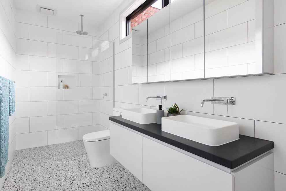 Photo of a contemporary master bathroom in Melbourne with flat-panel cabinets, white cabinets, an alcove shower, a one-piece toilet, white tile, ceramic tile, white walls, concrete floors, a vessel sink, grey floor, an open shower and black benchtops.