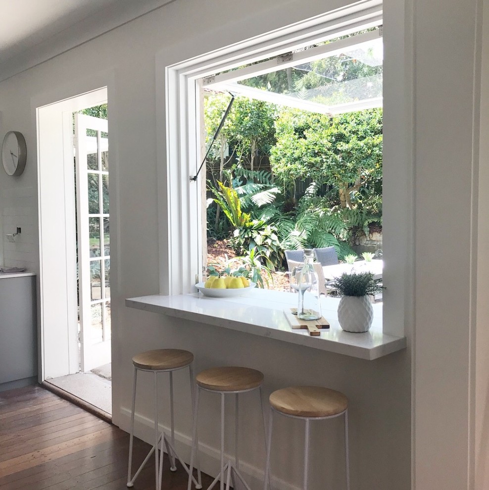 Mid-sized traditional u-shaped separate kitchen in Sydney with a farmhouse sink, shaker cabinets, grey cabinets, quartz benchtops, white splashback, ceramic splashback, stainless steel appliances, painted wood floors, no island, brown floor and white benchtop.