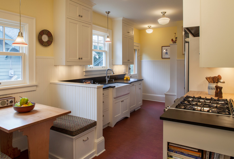This is an example of a small arts and crafts galley eat-in kitchen in Portland with a farmhouse sink, shaker cabinets, white cabinets, stainless steel appliances, no island, granite benchtops, black splashback, stone slab splashback and linoleum floors.