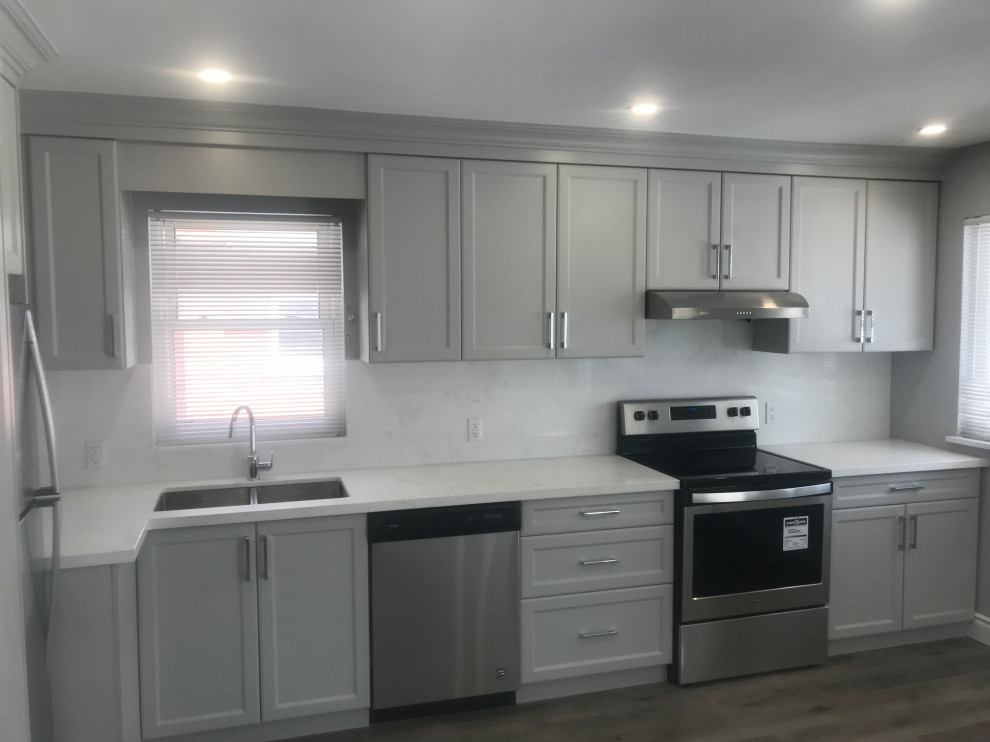 Example of a mid-sized transitional l-shaped medium tone wood floor eat-in kitchen design with an undermount sink, shaker cabinets, gray cabinets, quartz countertops, white backsplash, quartz backsplash, stainless steel appliances and white countertops