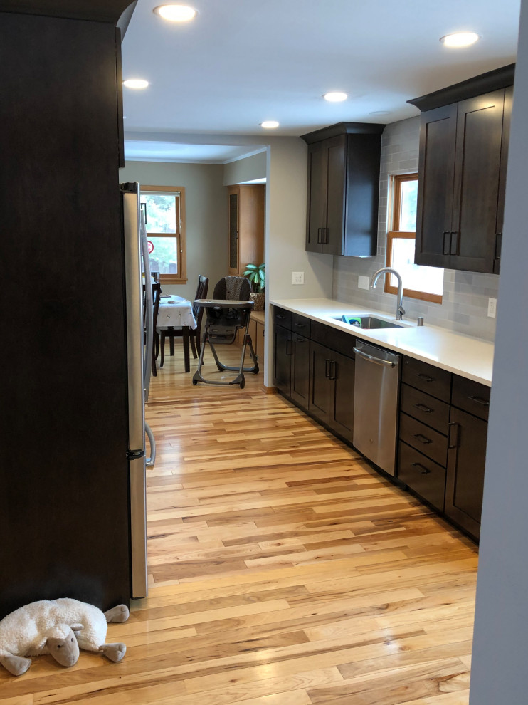 Inspiration for a mid-sized transitional galley light wood floor and brown floor eat-in kitchen remodel with an undermount sink, shaker cabinets, black cabinets, quartz countertops, gray backsplash, subway tile backsplash, stainless steel appliances, no island and white countertops