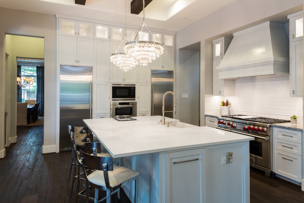 Mid-sized transitional kitchen in Houston with a farmhouse sink, recessed-panel cabinets, white cabinets, quartz benchtops, white splashback, subway tile splashback, stainless steel appliances, dark hardwood floors and with island.