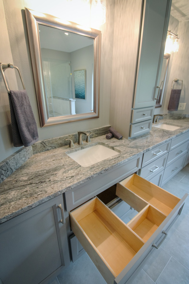 Photo of a large traditional ensuite bathroom in Milwaukee with shaker cabinets, grey cabinets, a one-piece toilet, grey tiles, porcelain tiles, grey walls, porcelain flooring, a submerged sink, granite worktops, grey floors, a hinged door, multi-coloured worktops, a shower bench, double sinks and a built in vanity unit.