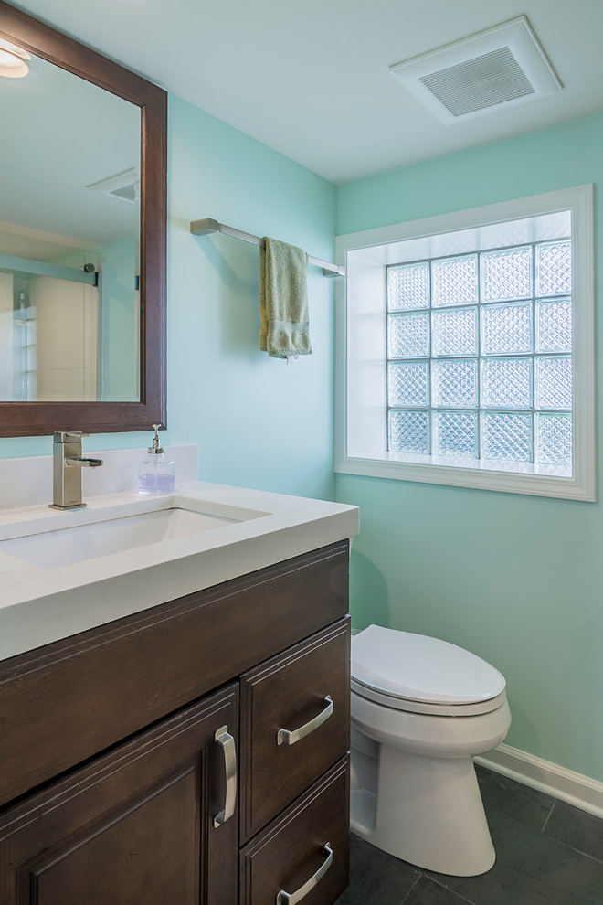 Design ideas for a small transitional bathroom in Chicago with raised-panel cabinets, dark wood cabinets, a drop-in tub, a shower/bathtub combo, a one-piece toilet, gray tile, blue walls, vinyl floors, a drop-in sink and engineered quartz benchtops.