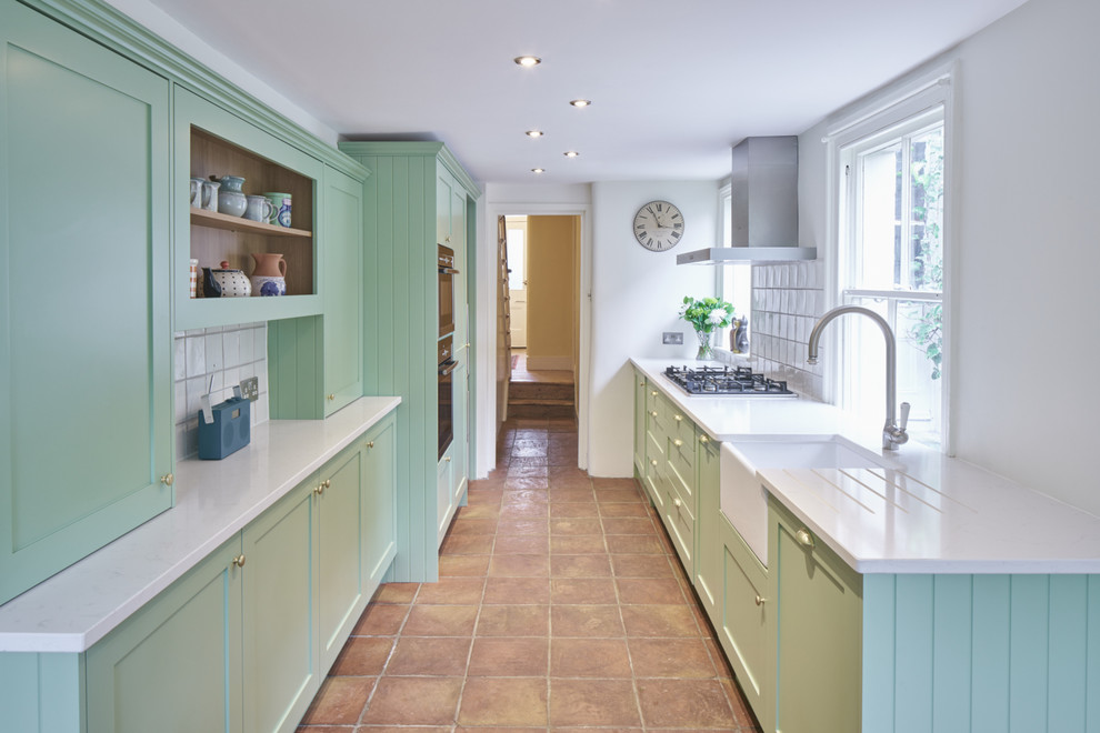This is an example of a small eclectic galley kitchen in London with a farmhouse sink, shaker cabinets, green cabinets, quartzite benchtops, white splashback, ceramic splashback, panelled appliances and terra-cotta floors.