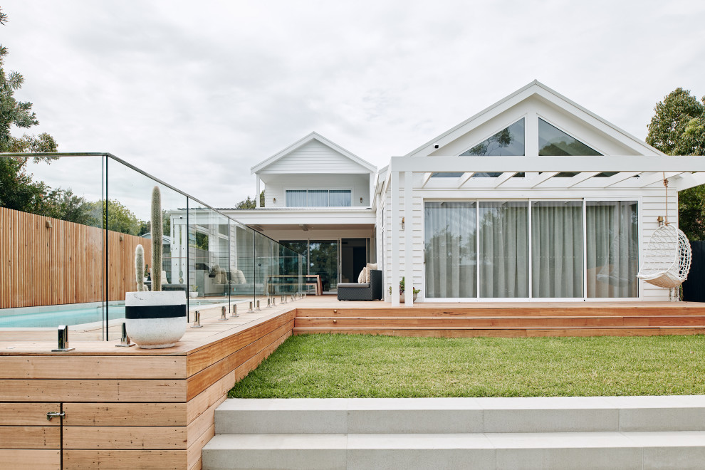 This is an example of a large beach style two-storey white house exterior in Melbourne with concrete fiberboard siding, a gable roof and a metal roof.