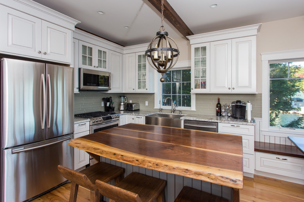 Inspiration for a mid-sized traditional separate kitchen in Boston with a farmhouse sink, glass-front cabinets, white cabinets, quartzite benchtops, beige splashback, glass tile splashback, stainless steel appliances, medium hardwood floors and with island.