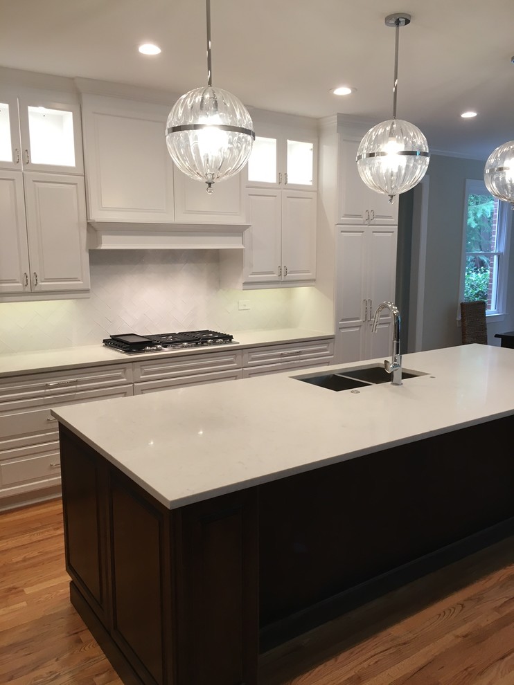 This is an example of an expansive transitional galley eat-in kitchen in Atlanta with an undermount sink, raised-panel cabinets, white cabinets, quartz benchtops, white splashback, ceramic splashback, stainless steel appliances, medium hardwood floors and with island.