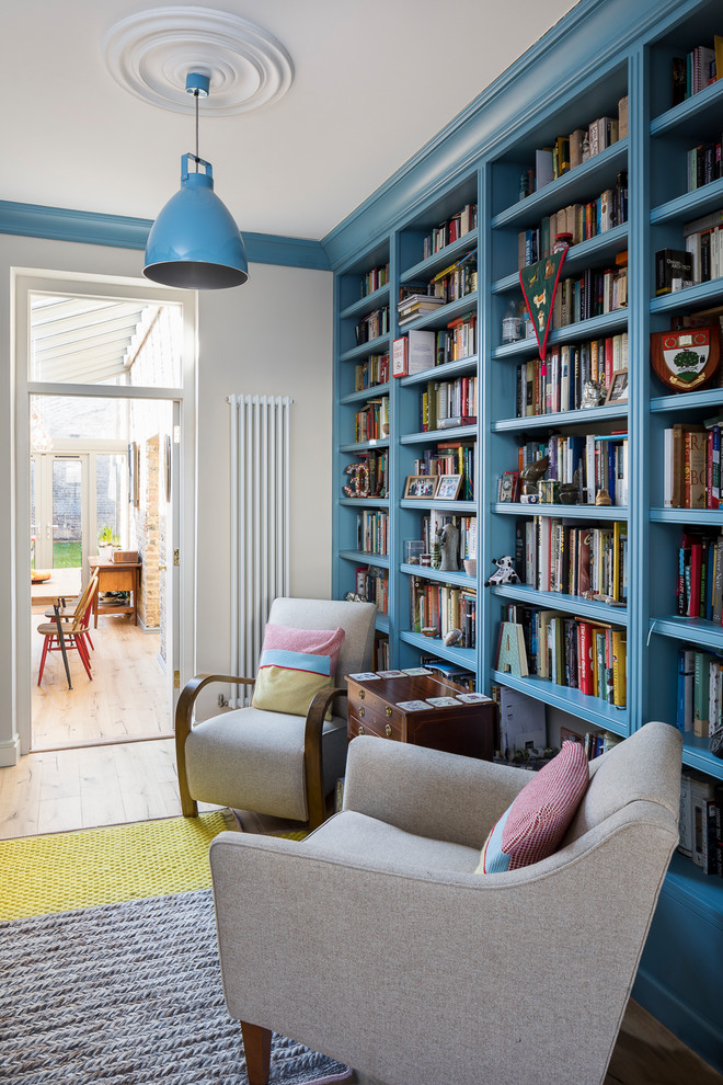 This is an example of a mid-sized transitional enclosed living room in London with a library, beige walls, light hardwood floors and brown floor.